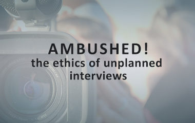 Decorative title image for "Ambushed! the ethics of unplanned interviews" with the title over a faded image of a close up of a video camera.